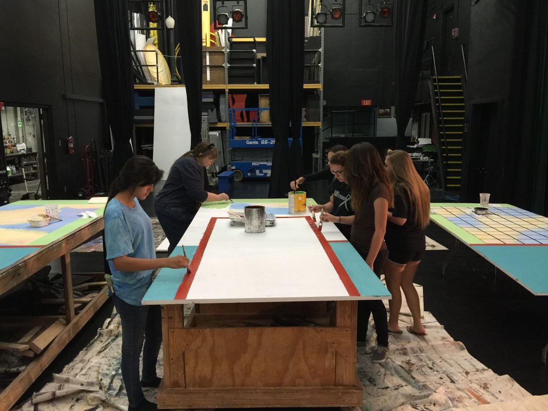 Students painting set pieces in the scene shop