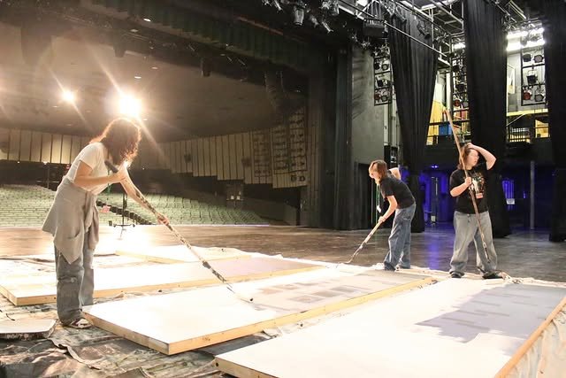 Students rolling paint on set flats on stage